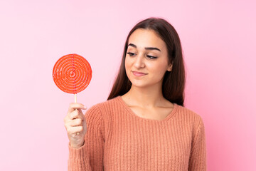 Young girl holding a lollipop over pink background with happy expression