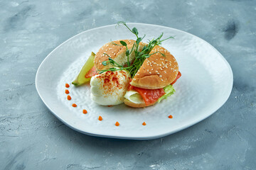 Perfect breakfast - salmon with poached egg and brioche bun in a white plate on a gray background. Eggs Benedict with seafood