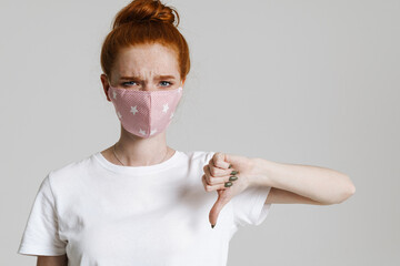 Photo of ginger confused girl in face mask showing thumb down