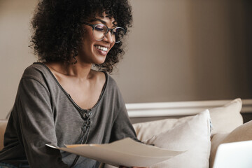 Naklejka premium Image of smiling african american woman working with papers while sitting on sofa