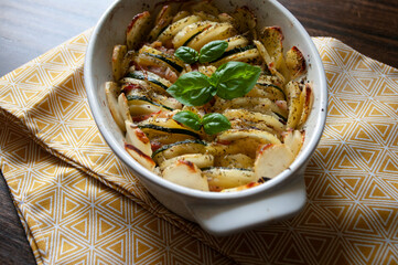 Hearty potato gratin bacon and zucchini,freshly served from the oven on a yellow tablecloth.Casserole food,vessel.