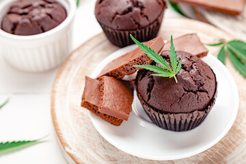 Marijuana chocolate cupcake muffins with weed cbd. Medical marijuana hemp drugs in food dessert. Weed muffins with cannabis, milk chocolate and cannabis leaves served on plate white table