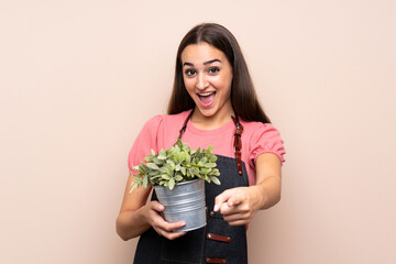 Young woman over isolated background taking a flowerpot and pointing to the front