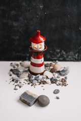 Small decorative lighthouse with sea shells and stones on dark background. Summer, holidays, vacation concept. Flat lay, top view