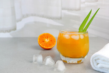 a glass of cool orange juice on the table near half of slice orange and  the curtain in the white bedroom during summer holiday in the luxury hotel in Thailand with happy family members