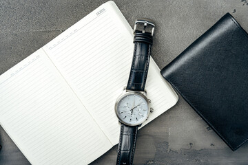 Businessman's accessories including notepad, watch and purse on dark grey background