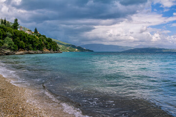 Beautiful landscape - turquoise colored sea water, golden sand, gray sky with dark stormy clouds and mountains on the horizon.