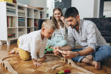 happy young family sitting floor and playing with wooden toy train at home