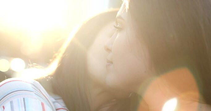 Two lesbian girlfriends outside with lens-flare kissing