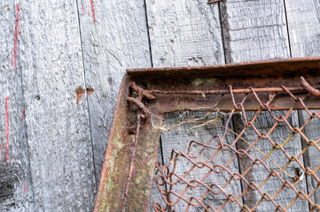 Old metal mesh covered in rust and an old wooden wall at the back, close-up, selective focus.