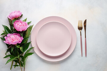 Pink peony flowers and a plate with cutlery on the table. Top view. Flat lay