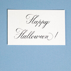 Calligraphic inscription Happy halloween on white textured paper, on blue paper card