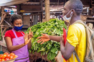 african woman in a local market wearing a face mask refusing to shake hands with someone