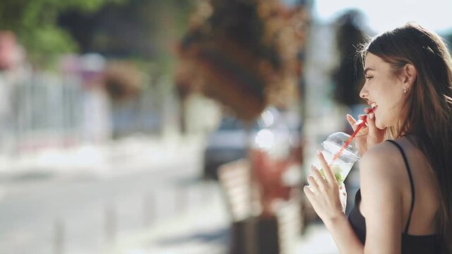 Cute girl drinks a drink through a straw. Medium shot. Slow motion.