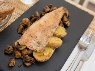 fried trout fillet on pillow of fried champignon mushrooms on dark warm stone plate