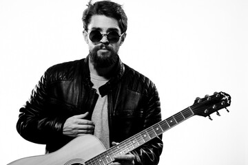 A man holds a guitar in his hands black leather jacket dark glasses music performance light background