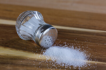 Ein Salzstreuer liegt auf einem hölzernen Brettchen, davor etwas Salz