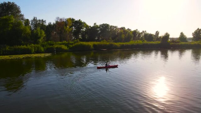 Young female traveller floats in kayak on river at warm ening sunlight