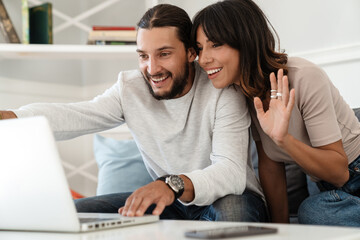 Image of cute cheerful couple using laptop and waving hand