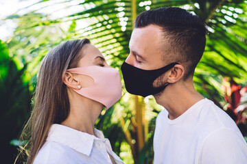 Young caucasian romantic couple kissing through medicine protection masks preventing covid-19 spread during pandemy, love feelings during world wide lockdown and quarantine with social distancing