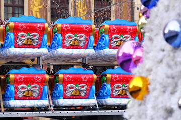Santa's plastic sleigh in a row near a decorated Christmas tree prepared for installation on children's attraction.