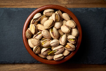 Ceramic bowl with pistachios on a wooden base.
