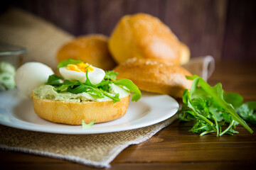 Homemade bun with cheese spread, fresh arugula and boiled egg in a plate