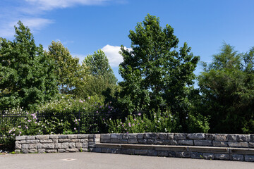 Fototapeta na wymiar Empty Stone Bench at Southpoint Park on Roosevelt Island during the Summer with Green Trees and Plants