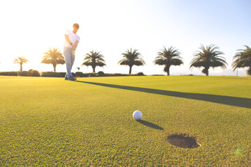 Golf club and ball in grass at the Golf course. White Golf ball on Green field golf course in morning time with sun light. Professional golf player fell Excited putting golf ball on green