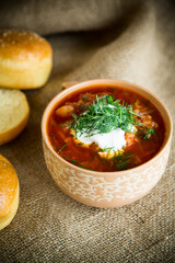 hot beetroot soup with sour cream, herbs and rolls in a ceramic bowl