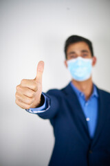 A man in suit with a mask showing his hand and a slightly tilted thumbs up. Concept of approval