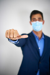 A businessman wearing a mask showing thumbs halfway, sign of uncertainty