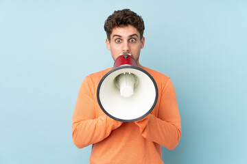 Caucasian man isolated on blue background shouting through a megaphone