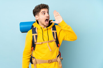 Young mountaineer man with a big backpack isolated on blue  background shouting with mouth wide open