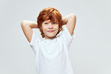 Cheerful red-haired boy holding hands behind his head smile white t-shirt 