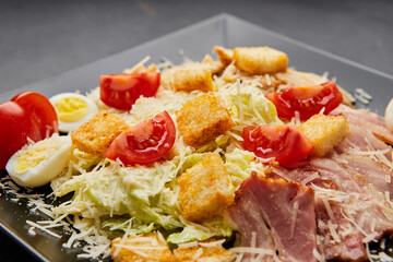 Caesar salad with lettuce, chicken, bacon and croutons on dark background
