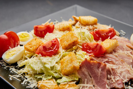 Caesar salad with lettuce, chicken, bacon and croutons on dark background