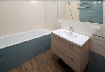 Fototapeta na wymiar Contemporary interior of modern bathroom. White sink with wooden drawers. Huge mirror. Hardwood floor.