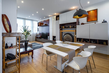 Luxury interior of living room with furniture in apartment. Chairs and table. White wall unit with Tibetian bowls and decorative gong.
