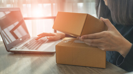 Woman hands holding a parcel box and using a laptop for business at home and laptop on background with copy space. Business start up SME concept.