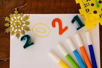 multicolored numbers of new year 2021 on white paper background with felt-tip pens, snowflake and watch