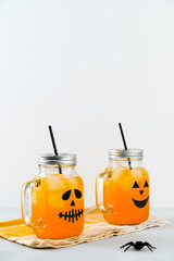 Iced pumpkin cocktails in glass jars decorated with scary faces on the gray table, white background. Halloween Party mocktails. Vertical orientation, copy space