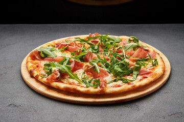 Delicious Italian Pizza with Parma ham and arugula, mozzarella cheese on dark background