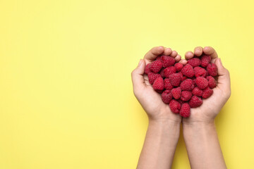 Woman holding delicious ripe raspberries on yellow background, top view. Space for text
