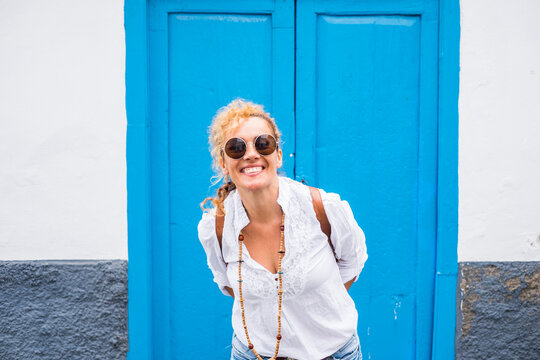 Portrait of cheerful and beautiful adult young caucasian woman smile and have fun in front of the camera and with blue door and white wall in background - home and people outdoor concept lfe
