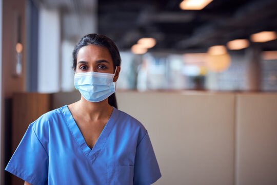 Female Doctor In Face Mask Wearing Scrubs Under Pressure In Busy Hospital During Health Pandemic