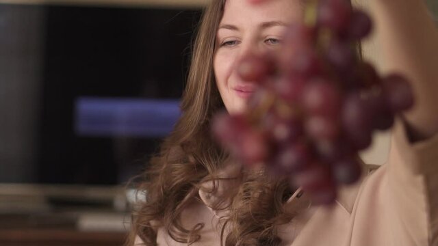 Woman eating red grapes at home. Hands hold a bunch of grapes and open the berries. High quality FullHD footage