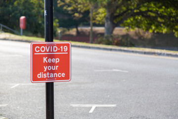 A sign reading Coviid-19 keep your distance attached to a lamppost