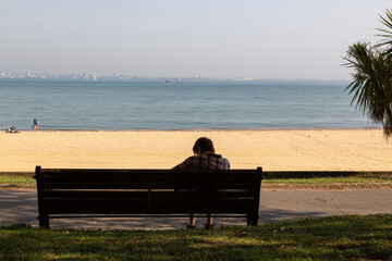 a woman sitting alone on a bench at the seaside or beach