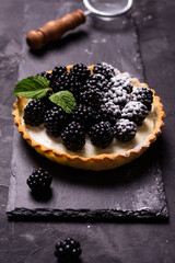 Berry tart with blackberry on a black plate